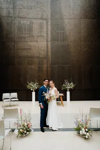 bride and groom posing in the north atrium of hackney town hall surrounded by flowers at their london wedding