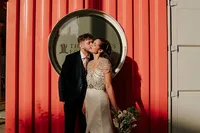 groom kissing bride on a cheek at their trinity buoy wharf wedding with red sea container in the background