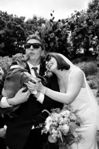 bride and groom holding a daschund dog, wearing sunglasses -black and white candid wedding photography