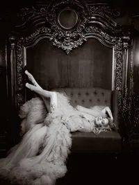 Black and white portrait of a woman in white faux fur on an ornate carved bed, luxury boudoir photography