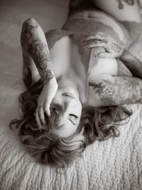 Black and white portrait of a woman lying on a fur rug with arms overhead, fine art boudoir photography