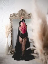 Woman in a black gown holding a pink bouquet in front of an ornate gold mirror, luxury boudoir photography