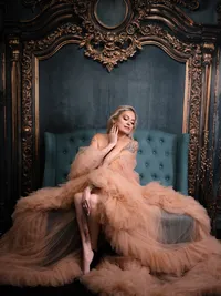 Woman in a peach tulle gown seated on a teal velvet chair in front of an ornate frame, luxury boudoir photography