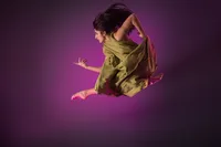 A woman in a green dress leaps gracefully in midair against a purple background, her hair and dress flowing in motion—a stunning image captured by a creative portrait studio Washington DC known for dynamic dance photography.