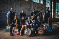 A band sitting and standing around a couch holding their instruments
