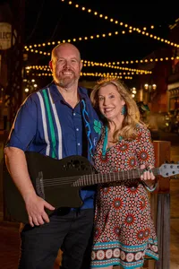 Two people smiling together while one holds a guitar