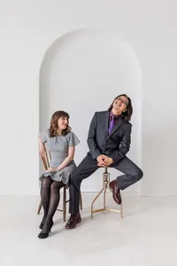A woman in a gray dress smiles at a man in a dark suit and purple tie, playfully seated sideways on a stool—an editorial portrait photography Washington DC metro session captured by a white arched wall.