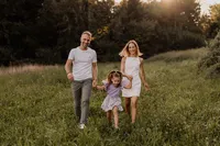 Familienfotografie Region Baden – Eltern gehen Hand in Hand mit ihrer Tochter durch eine Wiese