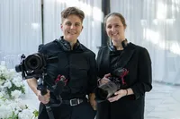 Two videographers standing together with their cameras smiling