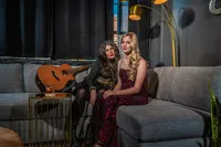 Two people sitting on a couch together with a guitar next to them