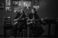 Two people with guitars sitting on stools playing together