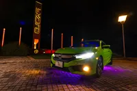 A green car parked outside at night with a purple under glow