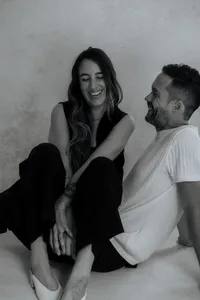 Two Cabo photographers in black and white sitting on the floor playfully draped over each other laughing