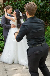 A videographer recording a couple in wedding outfits
