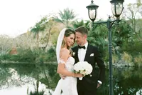 Bride and groom embracing outdoors by water, bride holding bouquet