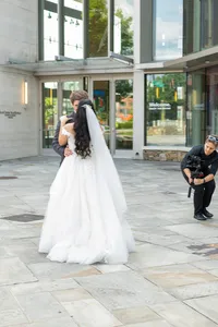 A newlywed couple kissing in front of a building while being recorded