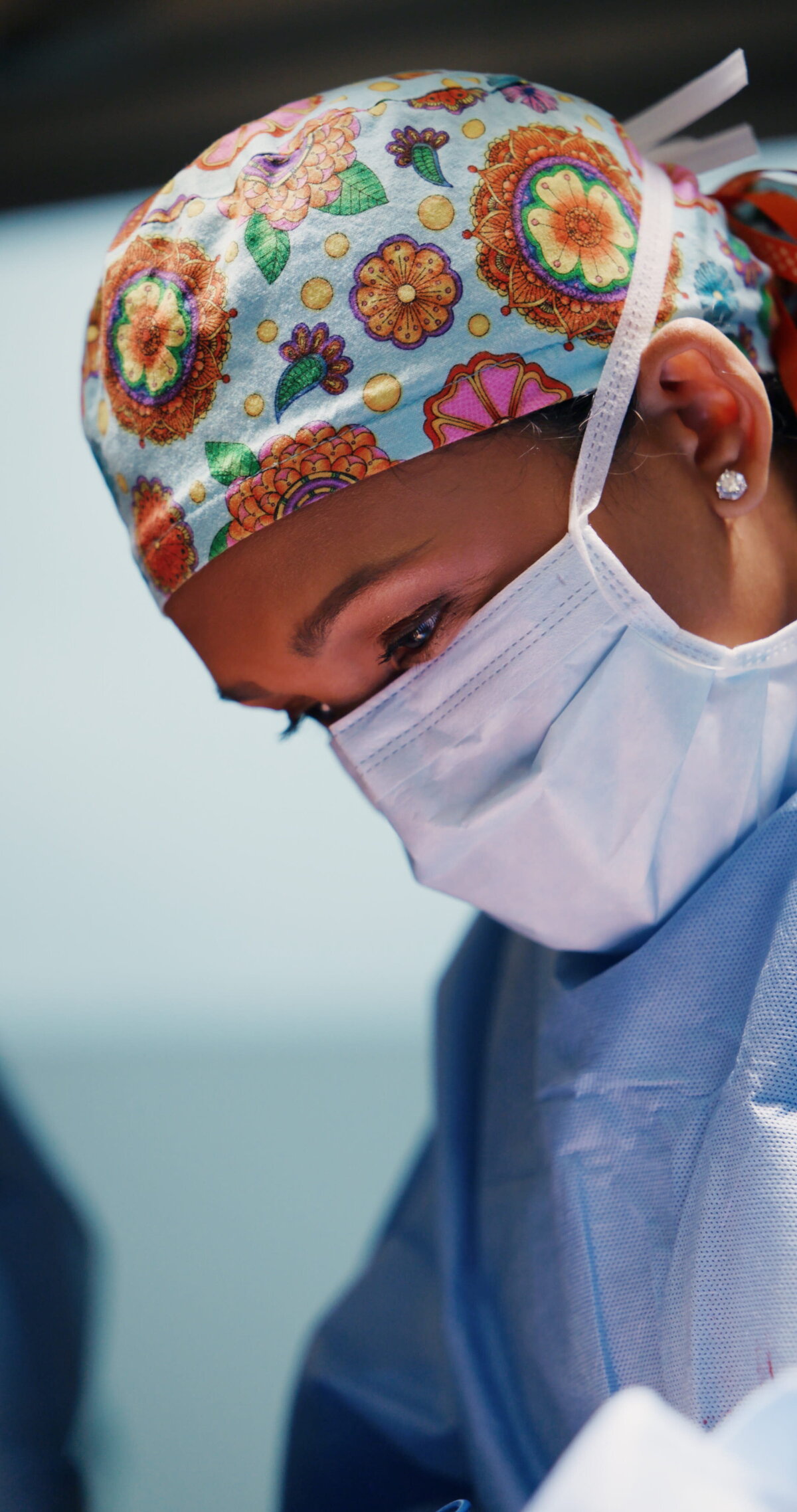 Surgeon in a floral scrub cap and mask looking down