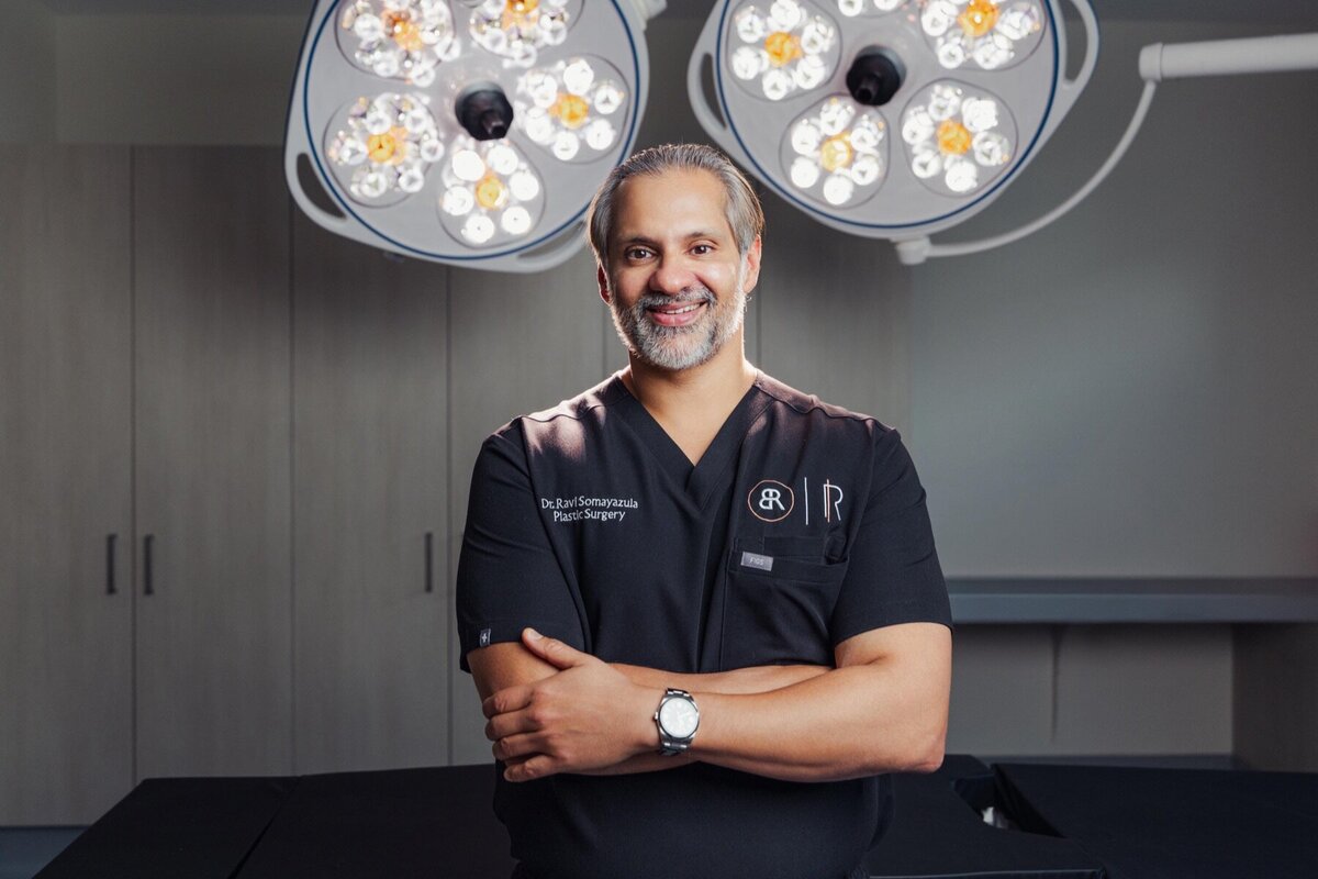 Body by Ravi doctor in black scrubs smiling under operating room lights