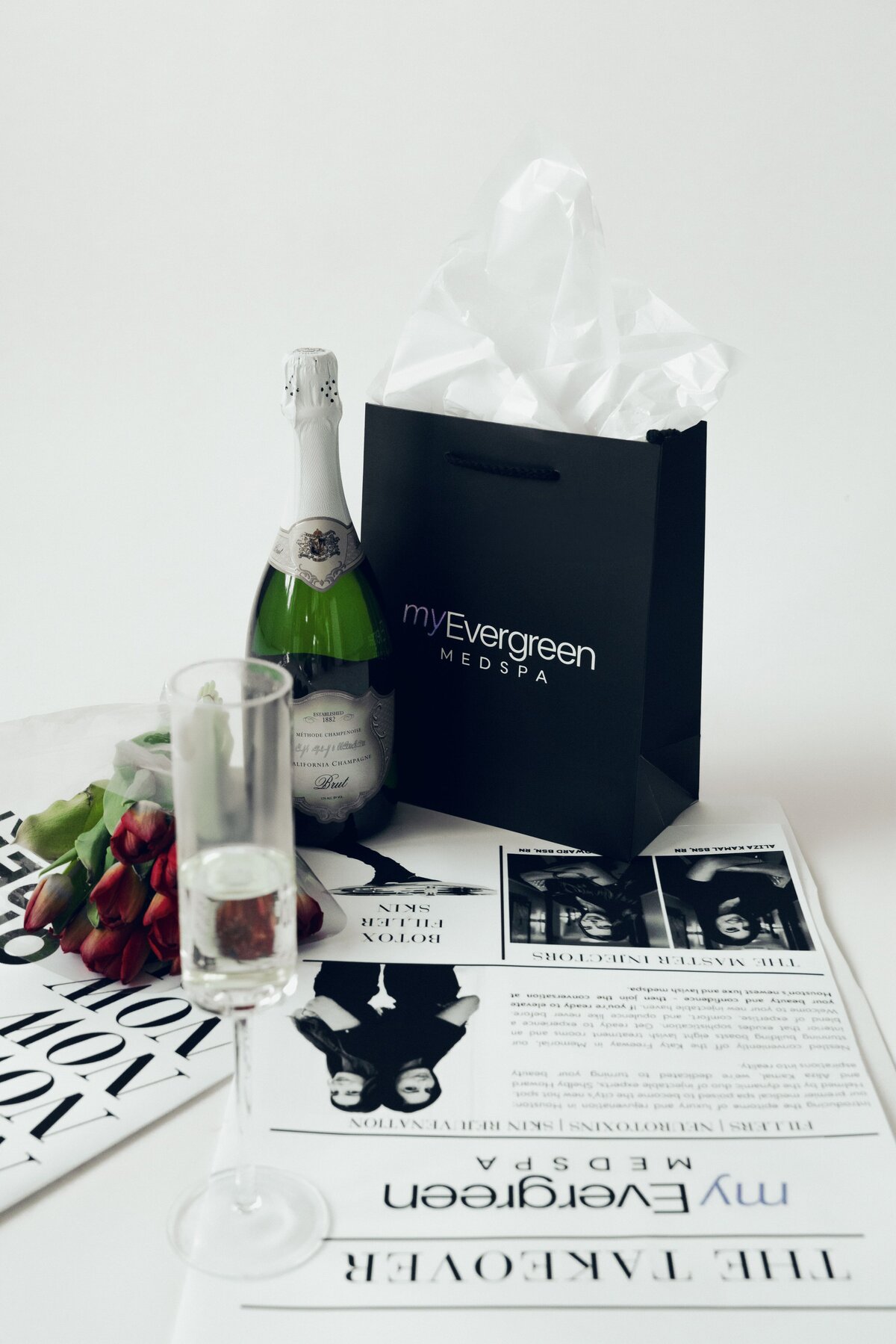 MyEvergreen MedSpa gift bag, champagne, and printed feature laid out for a brand photo