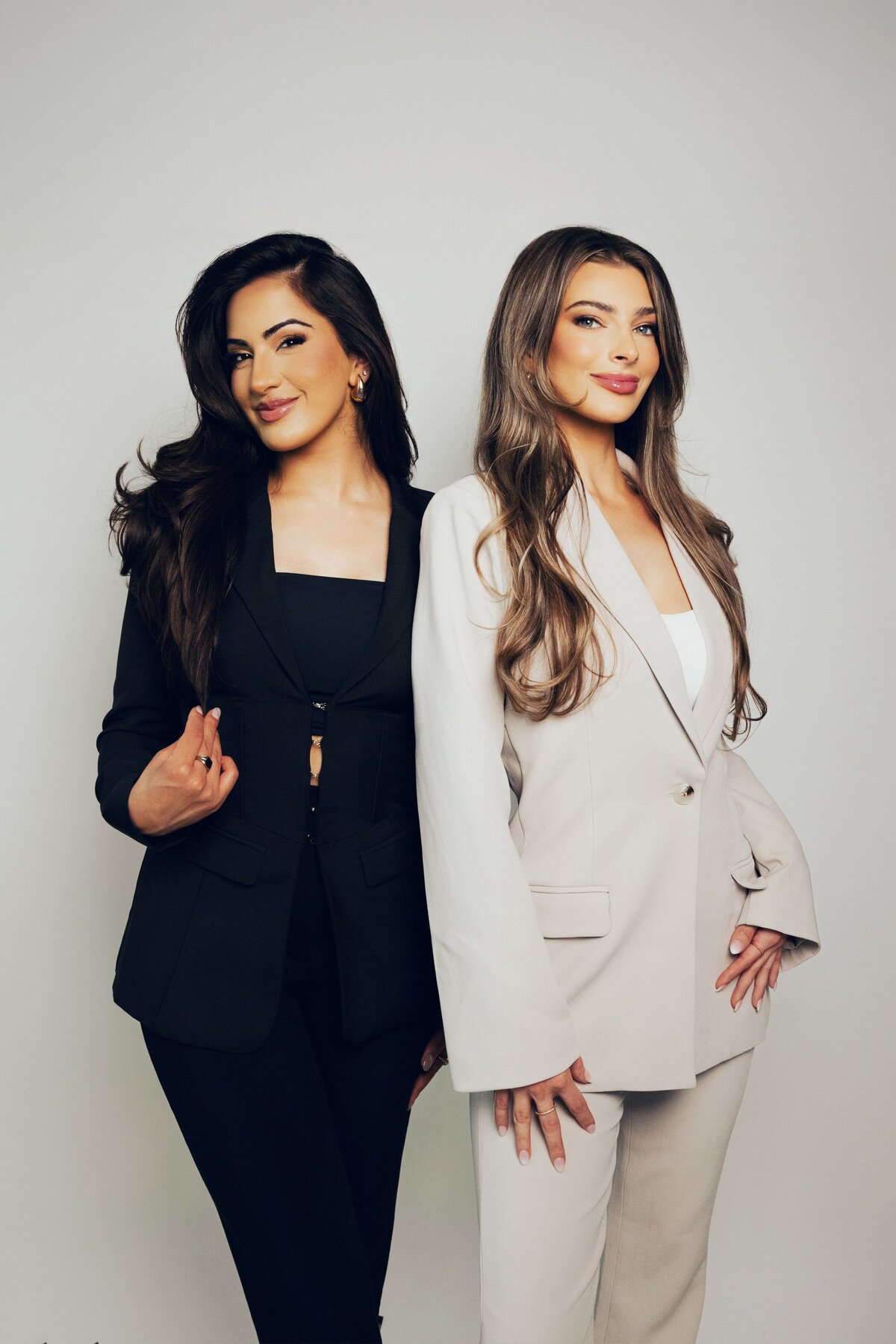 Two women in a black suit and a white suit posing for a brand photo