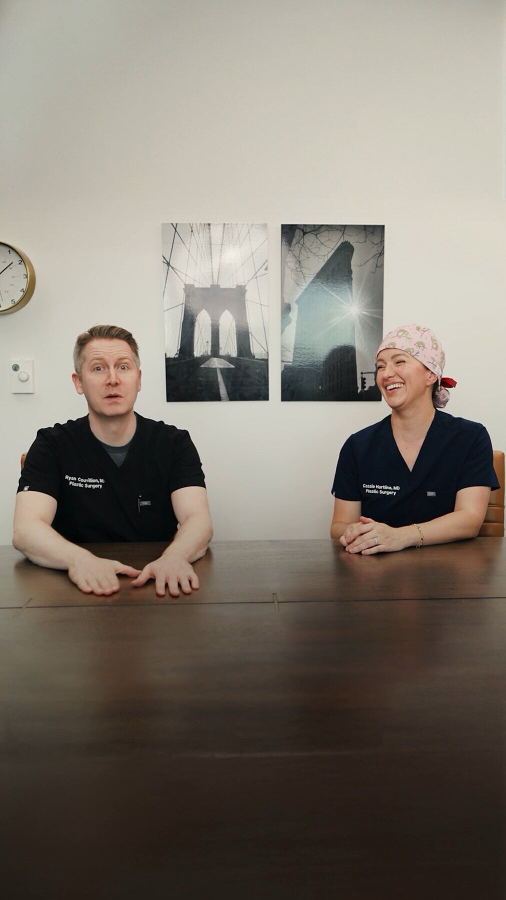 Two surgeons in black scrubs seated at a conference table