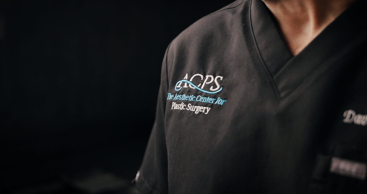 Close-up of a black scrub top with an embroidered plastic surgery practice logo