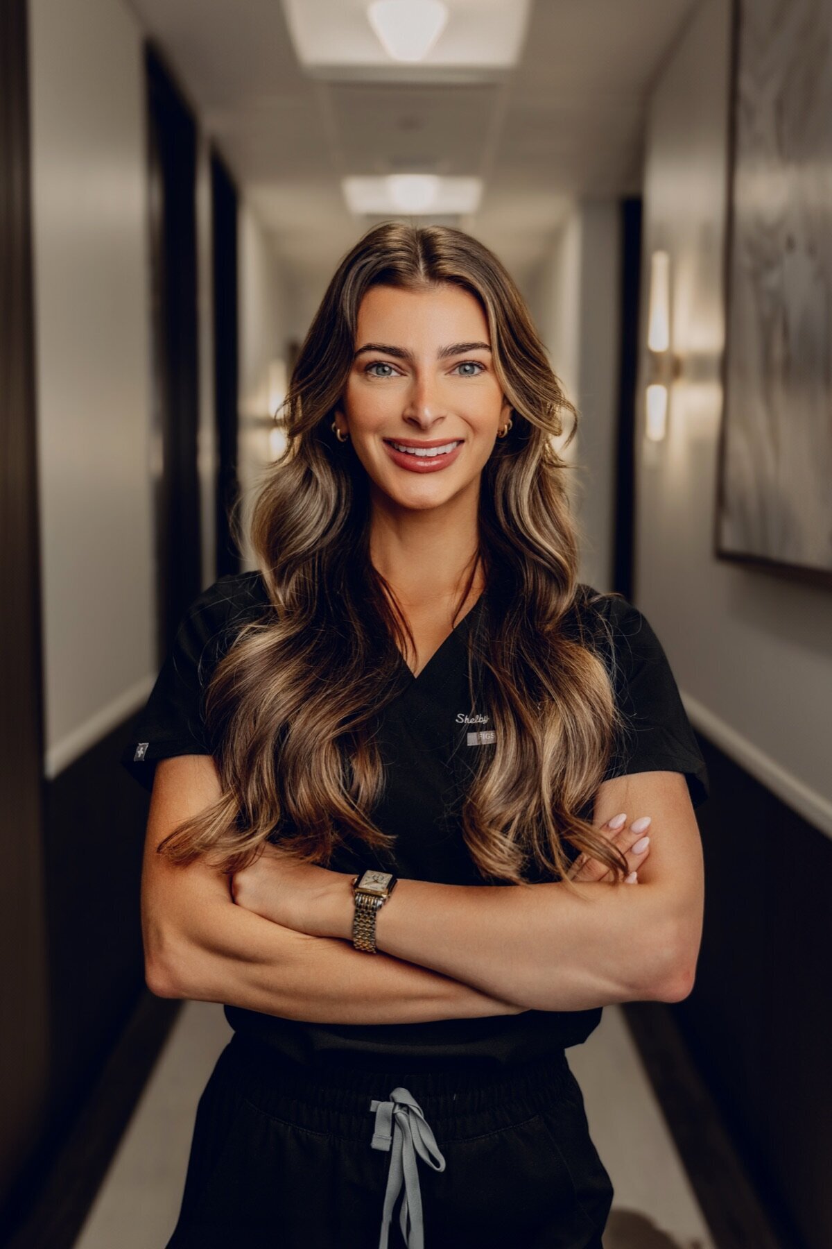 Team member in black scrubs with arms crossed in a hallway