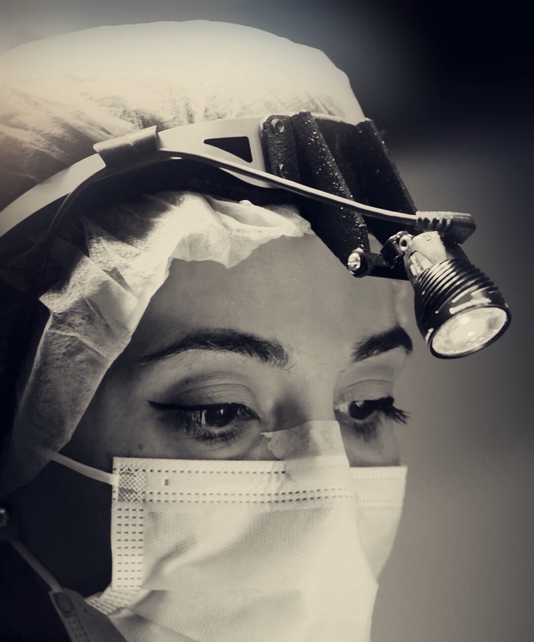 Black and white close-up of a surgeon in loupes and a mask