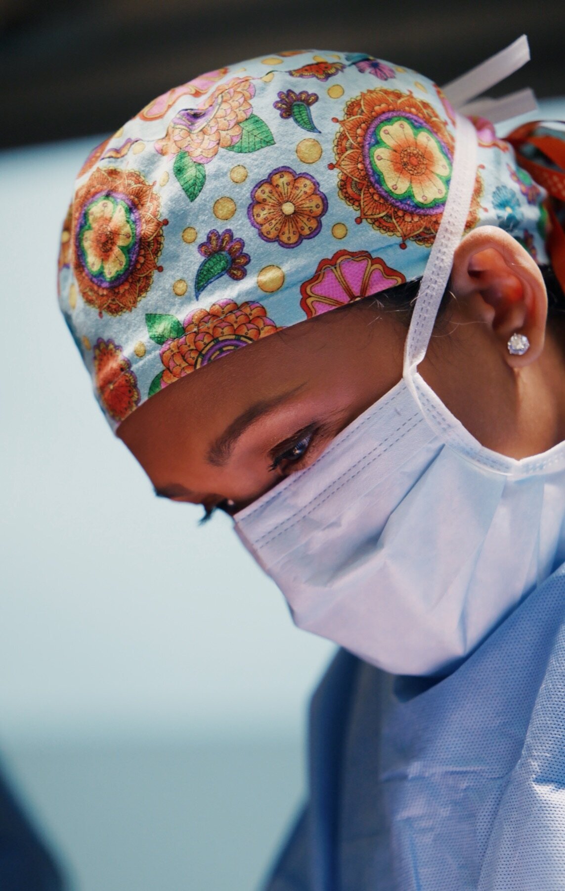 Surgeon in a floral scrub cap and mask looking down during a procedure