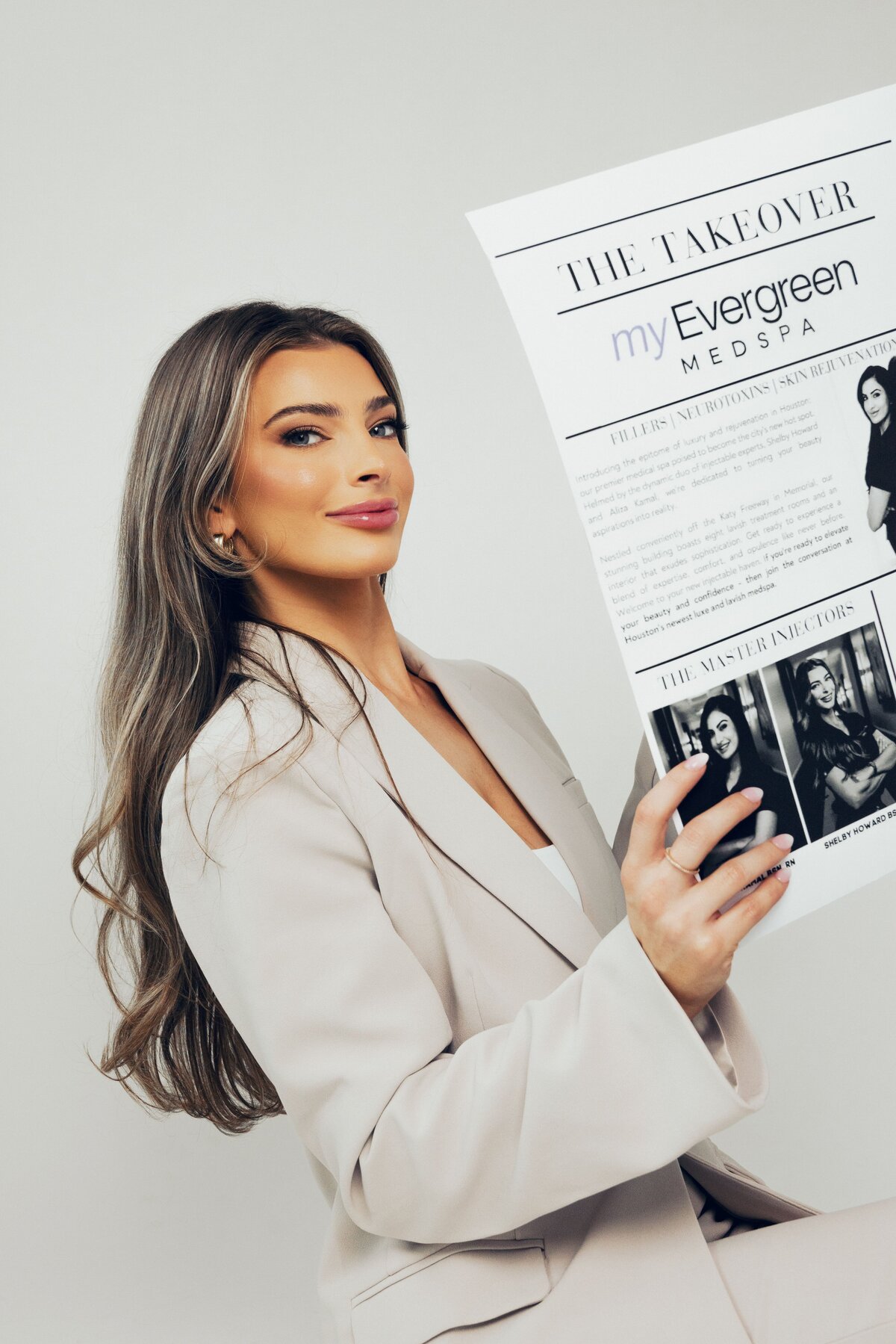 Woman in a white suit holding a printed feature about MyEvergreen MedSpa