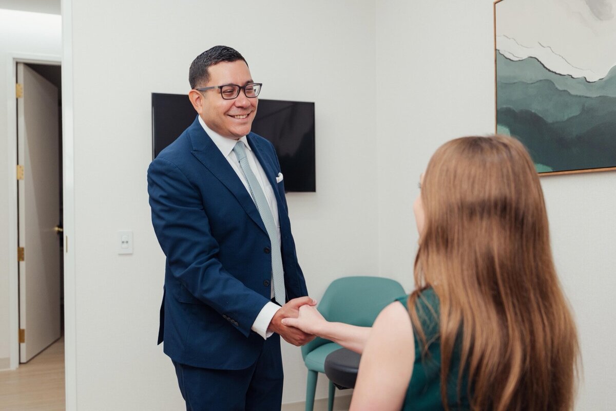 Man in a navy suit shaking hands with a patient in a consult room