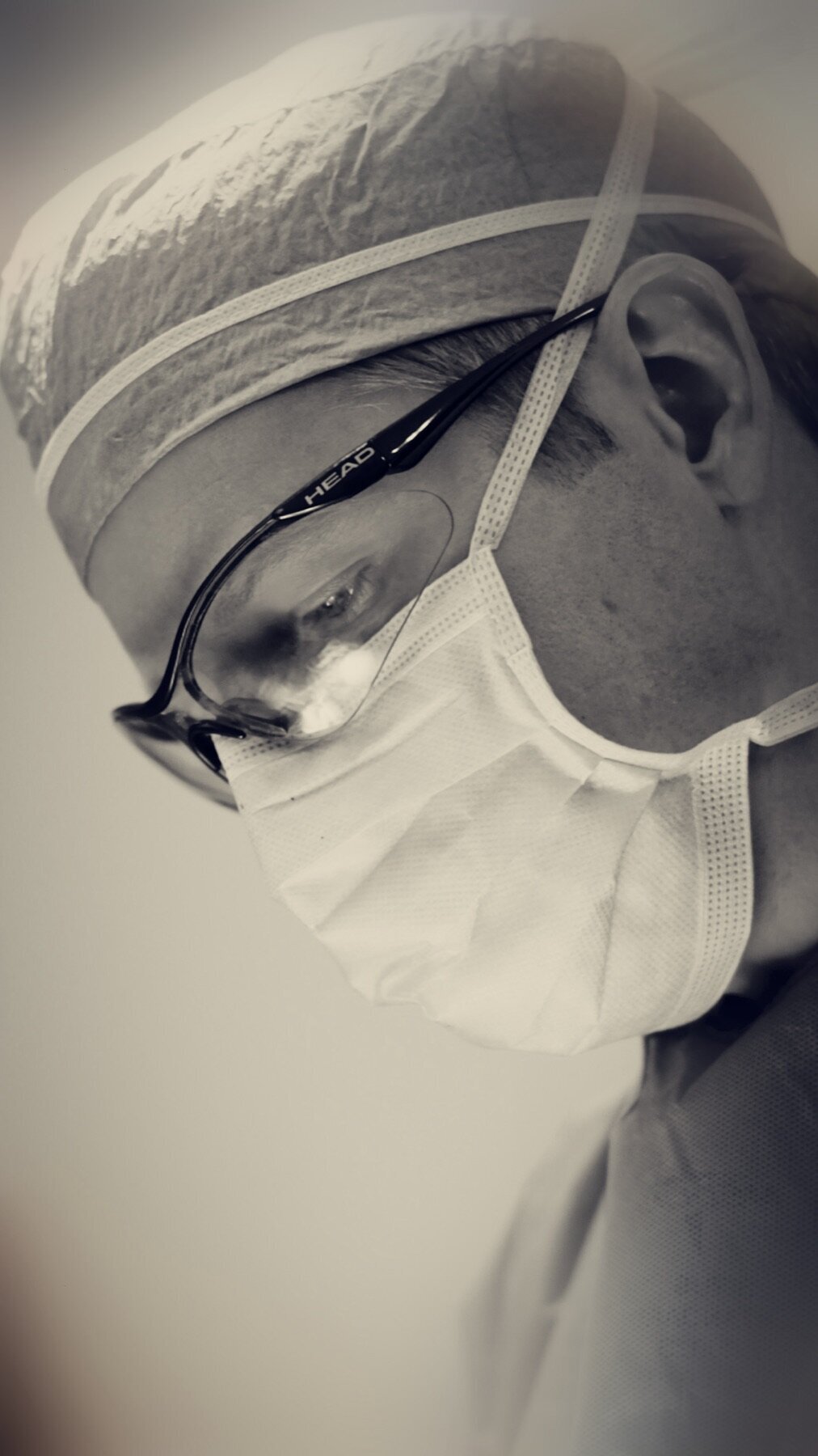Black and white photo of a surgeon in a mask and loupes