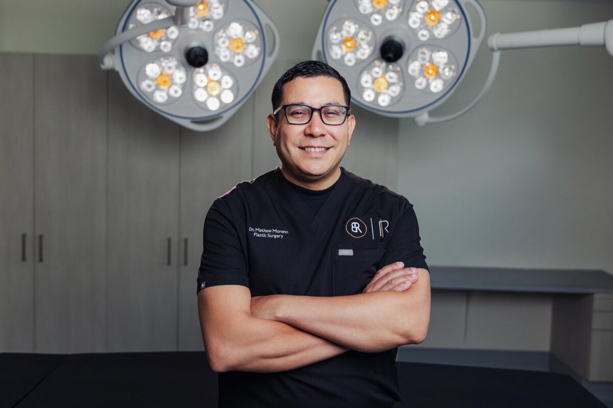 Body by Ravi doctor in glasses and black scrubs with arms crossed in the operating room