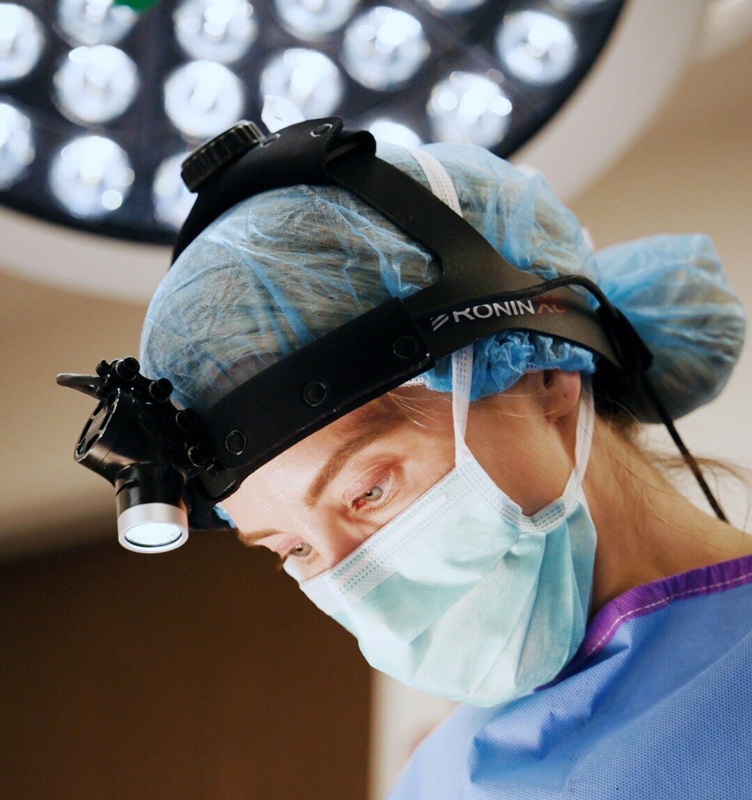 Surgeon in a headlight, cap, and mask looking down during a procedure