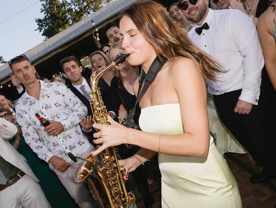Photo of a woman in a strapless gown playing the saxophone in the midst of an event.