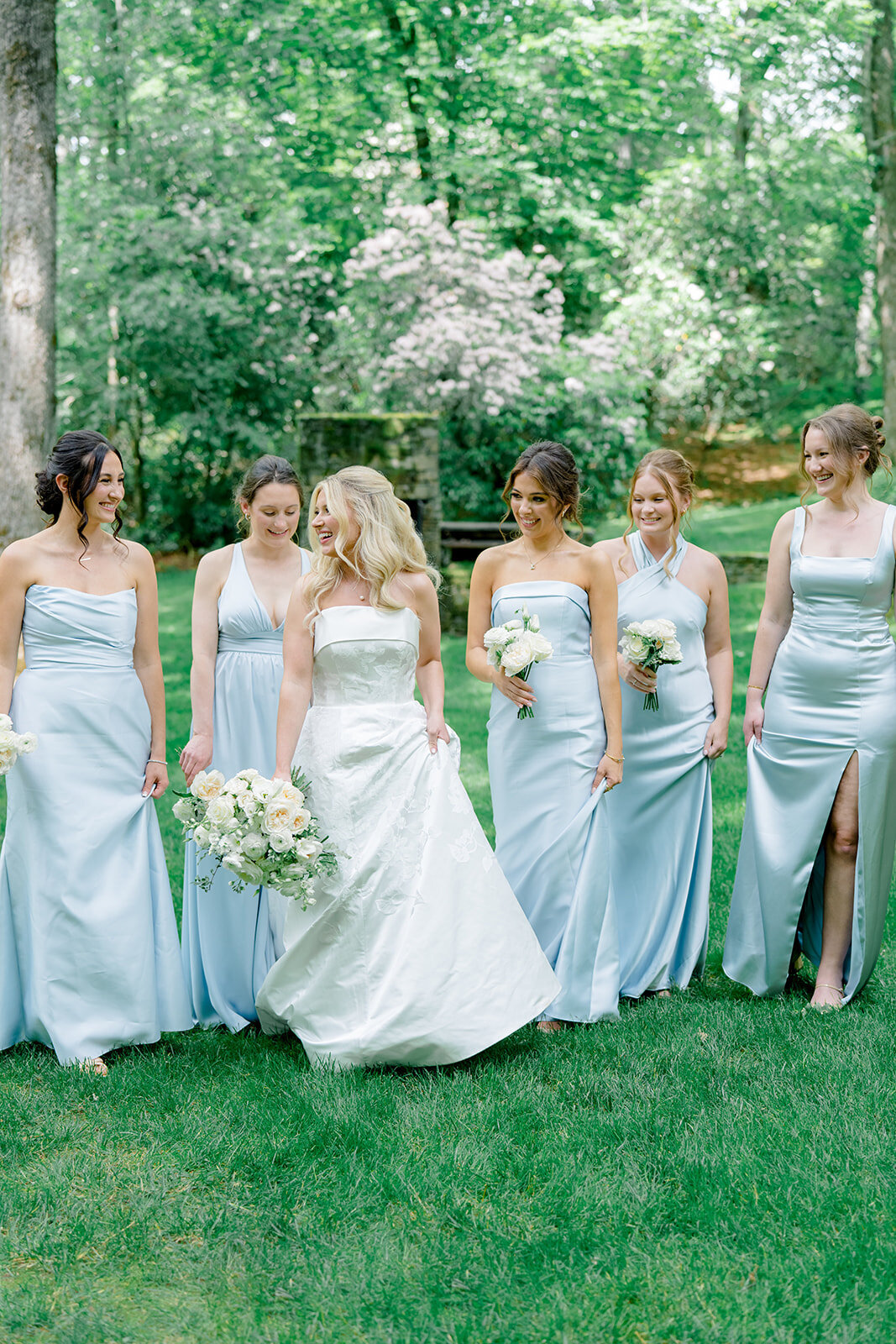 Bride walking and laughing with bridesmaids in light blue dresses during an outdoor garden wedding in Highlands, NC.
