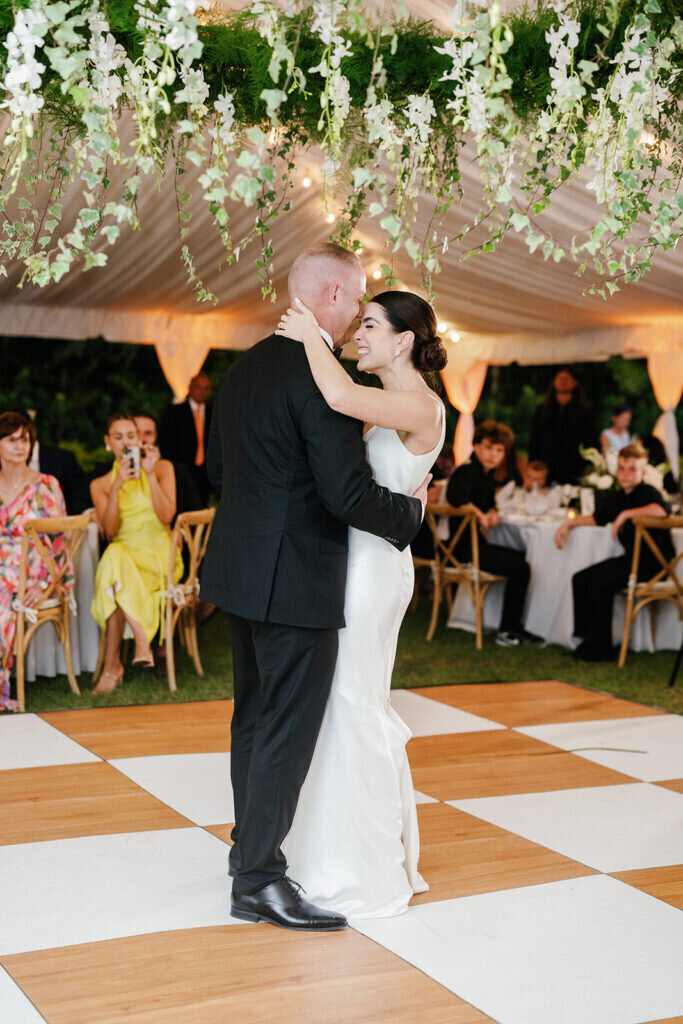 A joyful moment as the newlyweds share their first dance, smiling and embracing under a beautifully decorated reception tent with lush florals and warm lighting. Captured by Claudia Amalia Photography, a Florida Keys wedding photographer specializing in destination weddings.