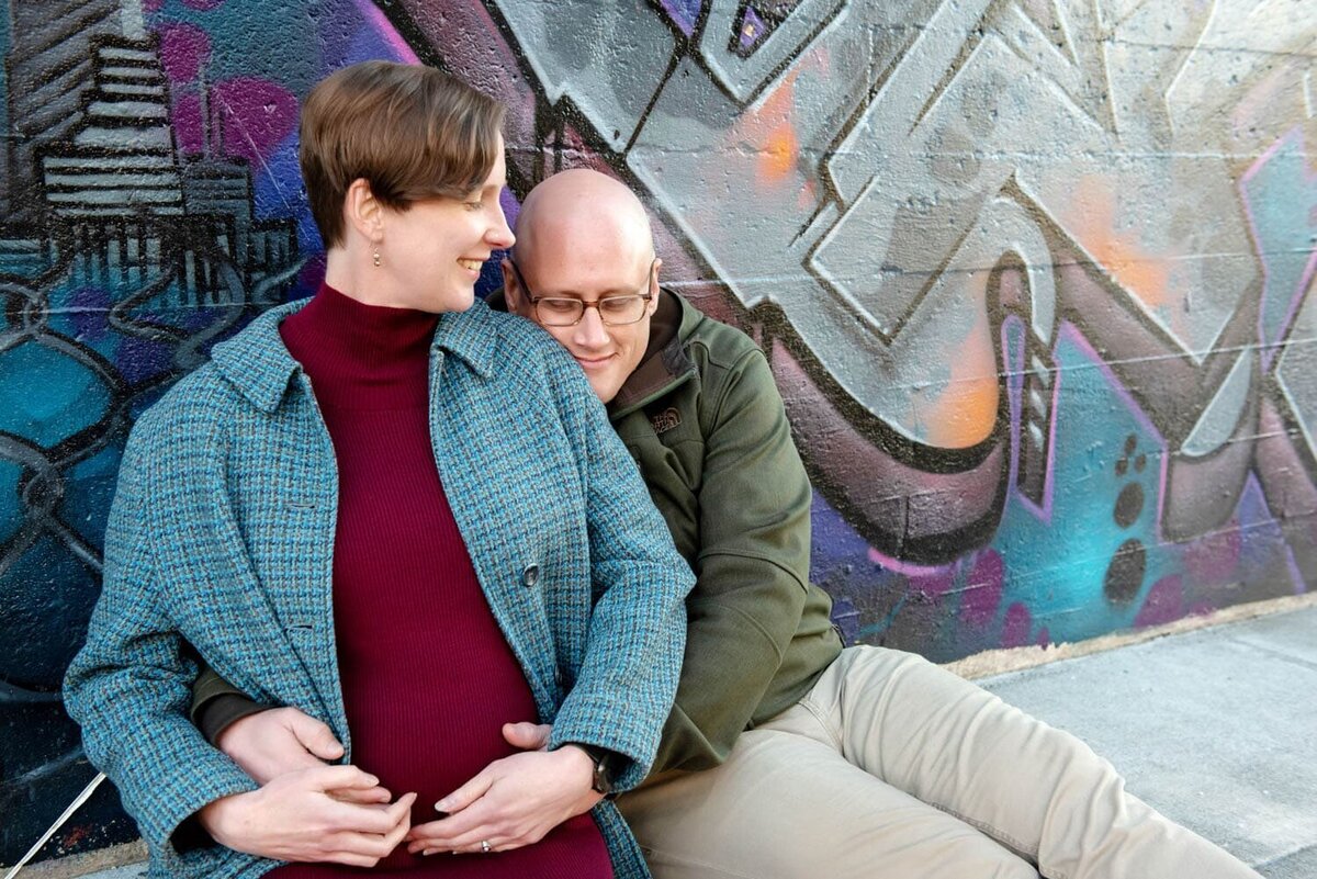 a man hugs a woman sitting on the ground in front of a graffiti mural