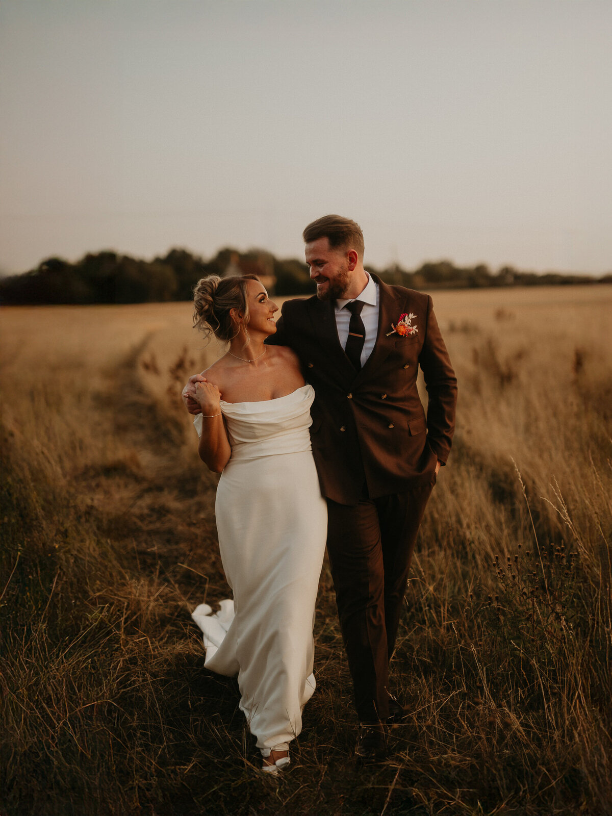 Bride and groom walk through the fields at Lapstone Barn during golden hour. 