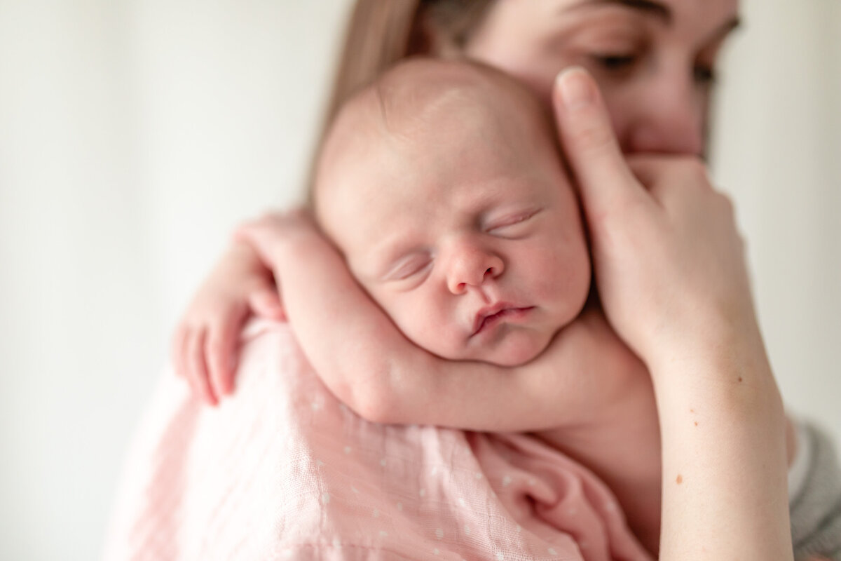 Newborn baby draping her arms over her mothers shoulder as mother holds her head gently