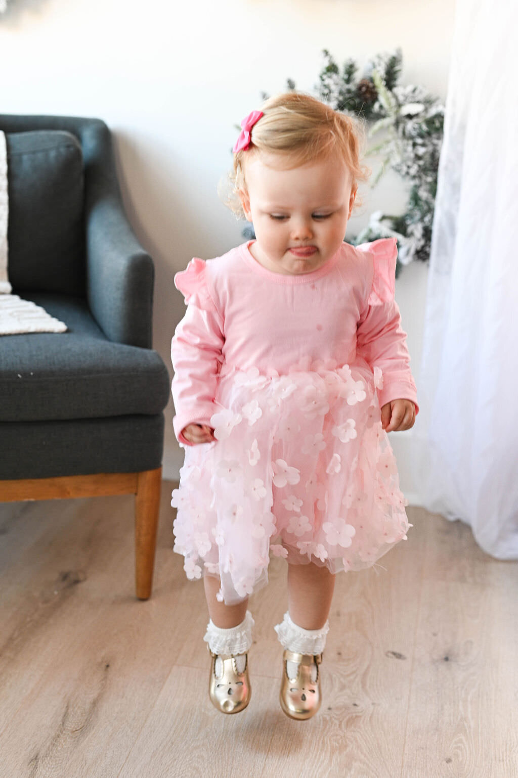A toddler in a pink dress jumping.