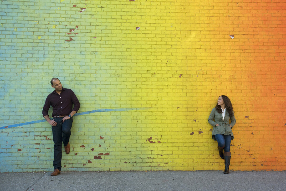 A couple standing on either side of a gradient colored wall 