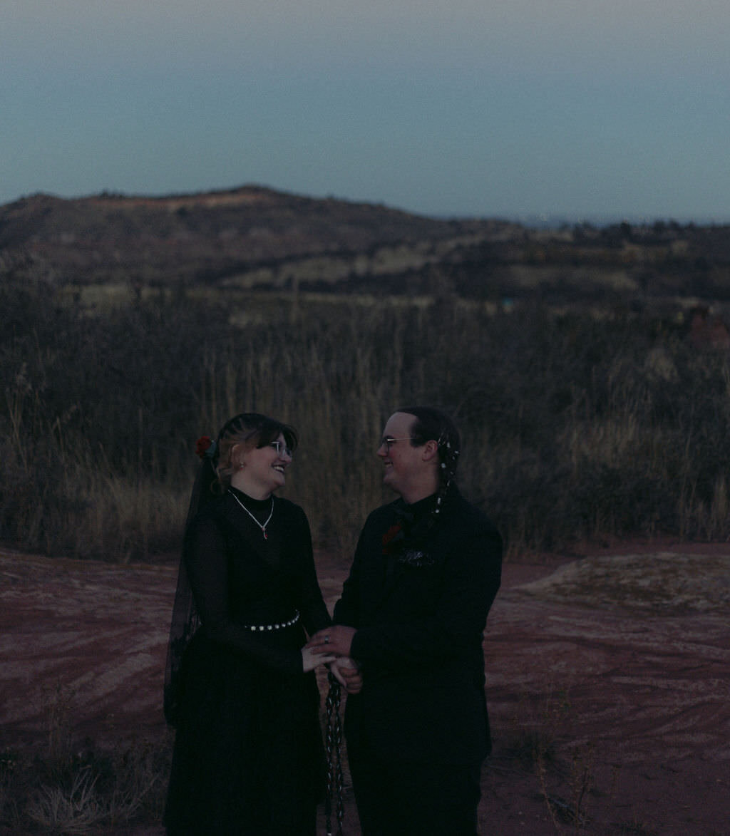 A wedding couple holding hands and smiling at each other.