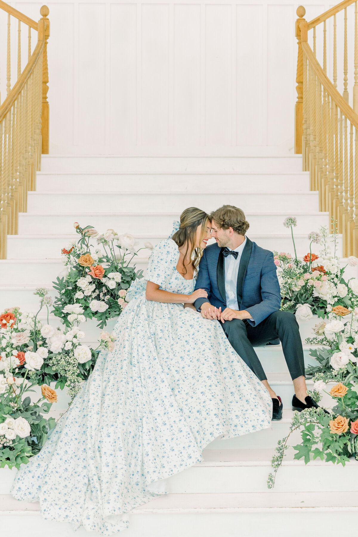 Bride in a floral white and blue wedding dress sharing an intimate moment with a groom in a blue suit