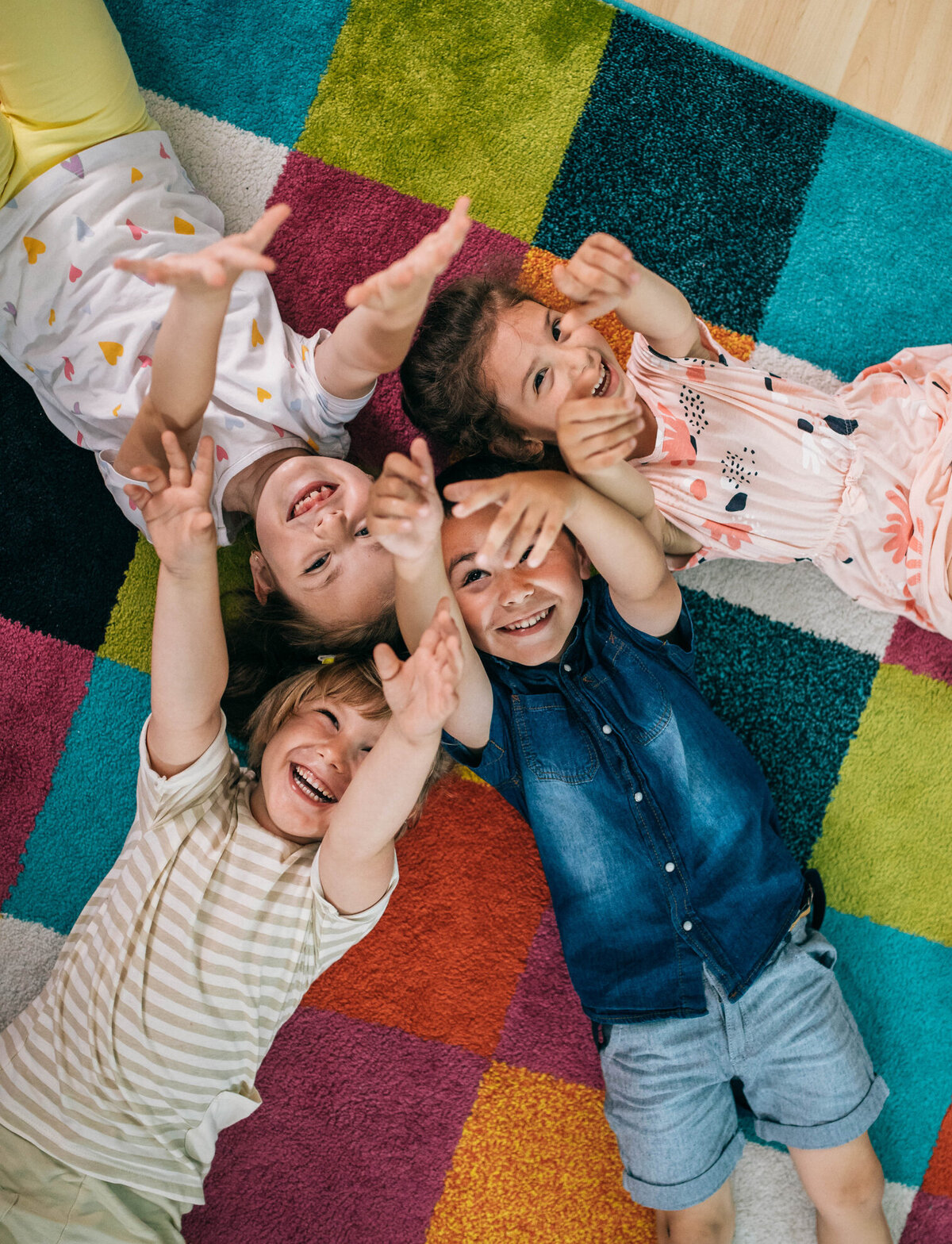 Aerial view of children smiling and raising their hands while lying on a colorful playmat