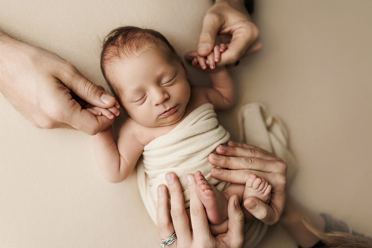 Adorable newborn baby boy laying on his back while mom and dad and holding his hands and feet.
