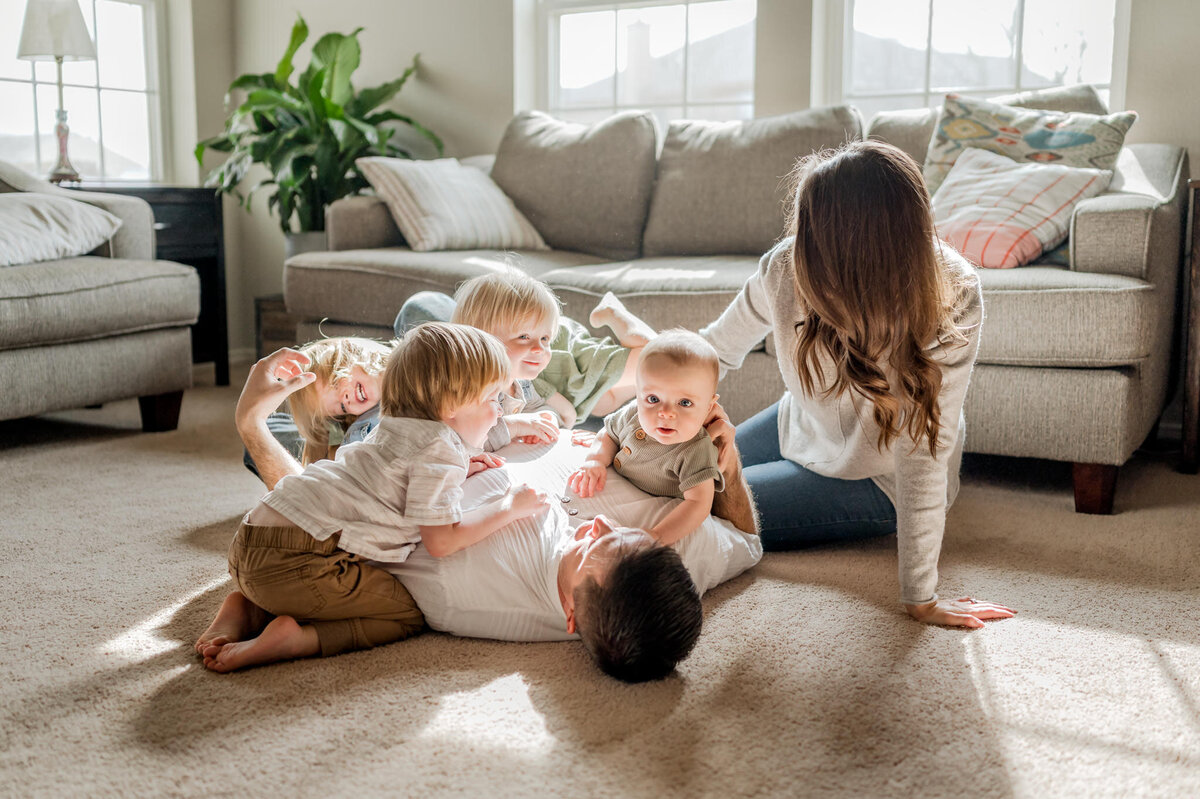 Big family with four under four wrestles on the floor of their living room during family photography by Cassey Golden.