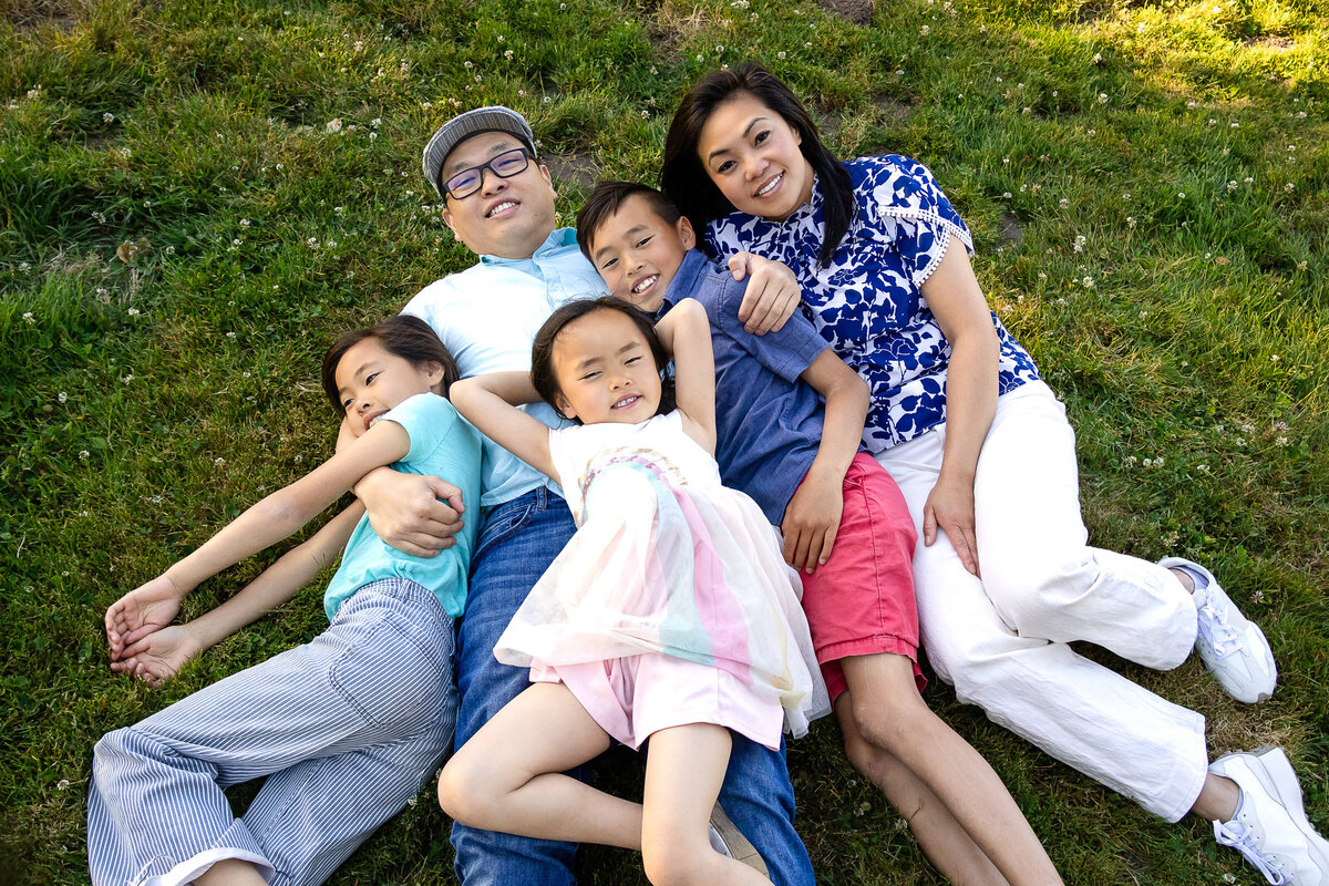 Golden hour portrait of a family of five lying down in rose garden – joyful, natural light family photography by Ellobelle Photography in the San Francisco Peninsula kohl mansion Burlingame