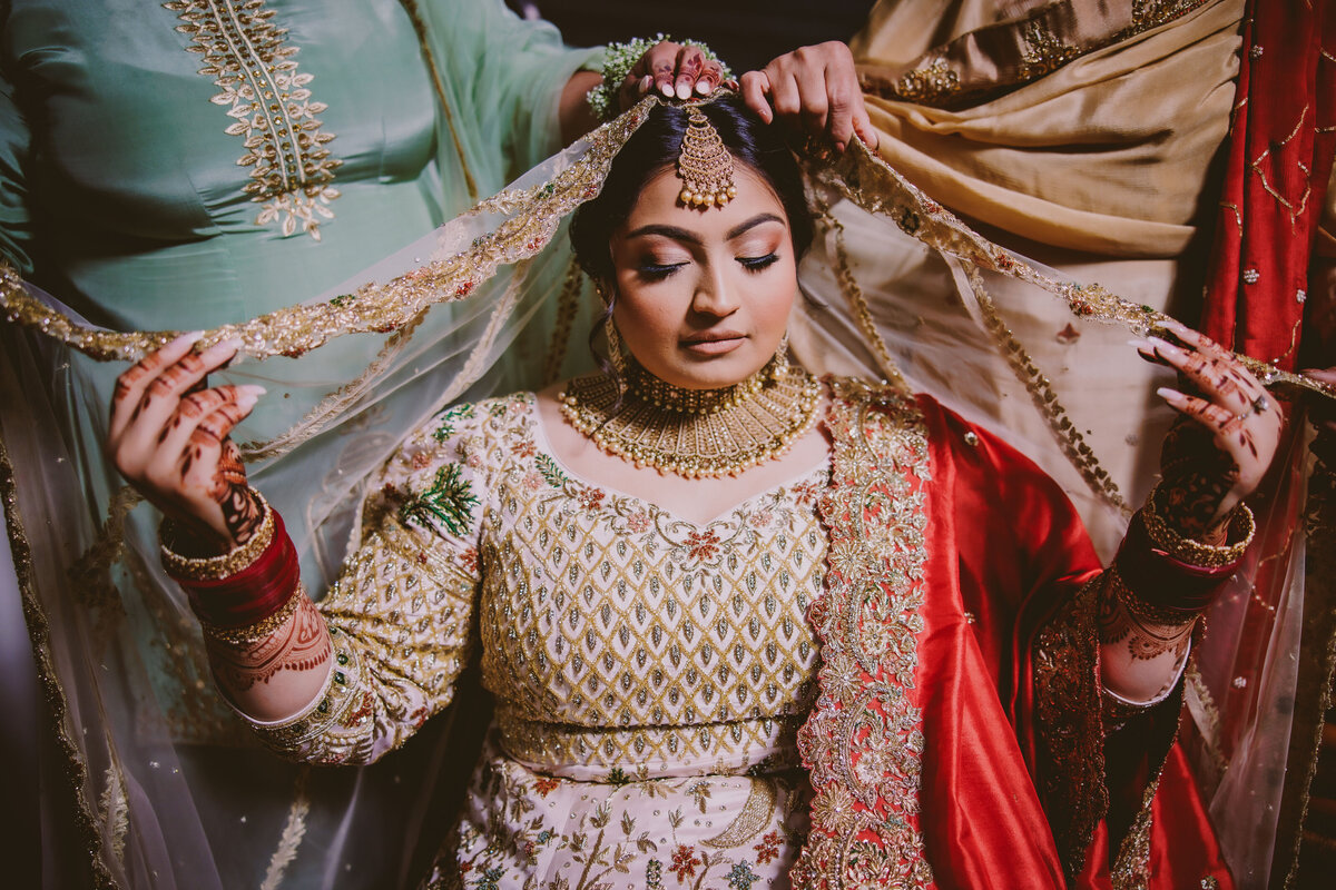 sikh bride getting the dupatta veil set on her head by her family before the wedding