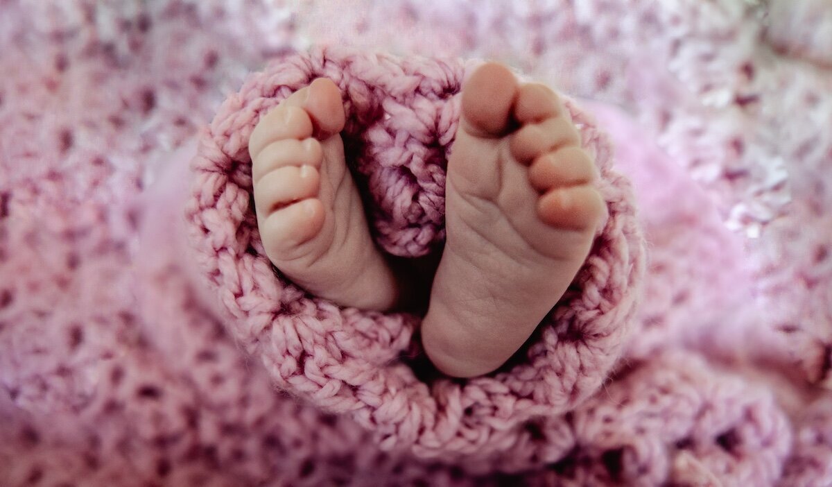 a closeup of a newborn baby's toes wrapped in a pink knitted blanket